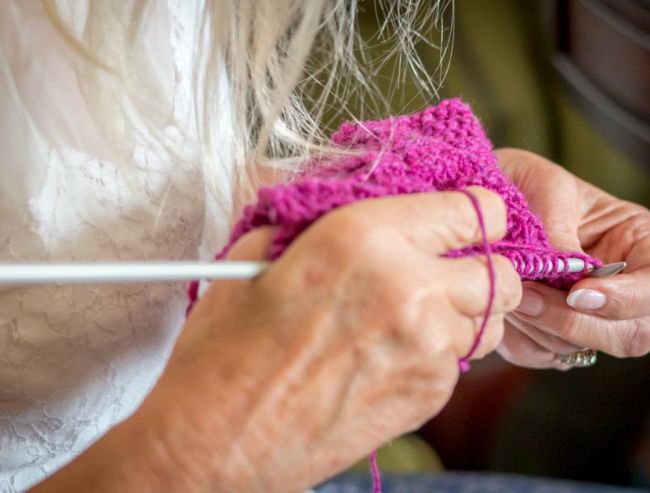 Close-up of a person's hands using long needles to knit a piece of vibrant pink yarn.