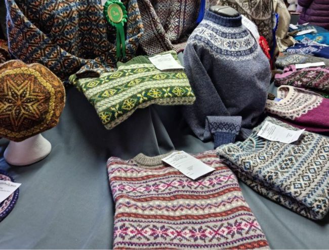 A collection of colorful, intricately patterned Fair Isle knit sweaters and a matching hat displayed on a table.