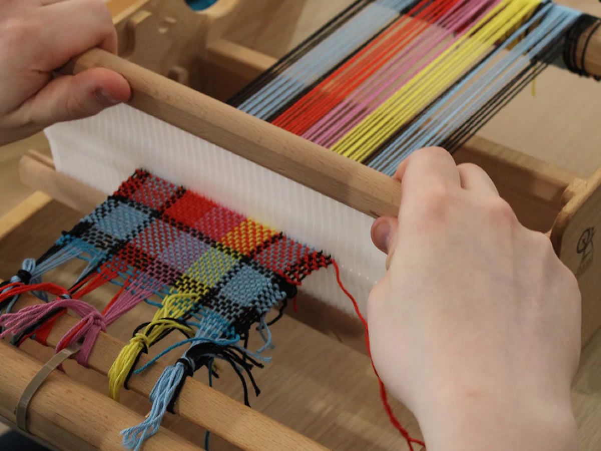 Hands weaving on loom.