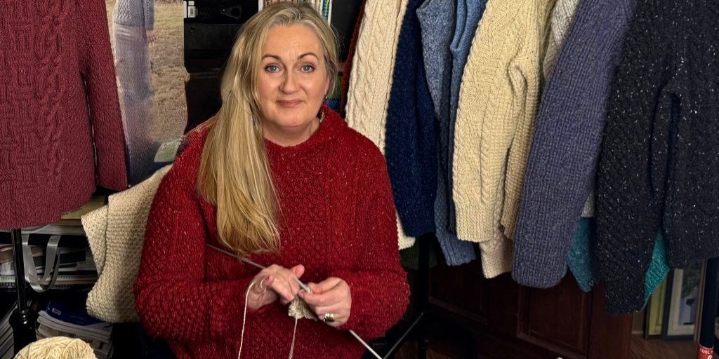 Knitter wearing Aran jumper surrounded by Aran sweaters