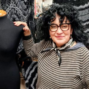 Woman with arm on mannequin and knitwear behind