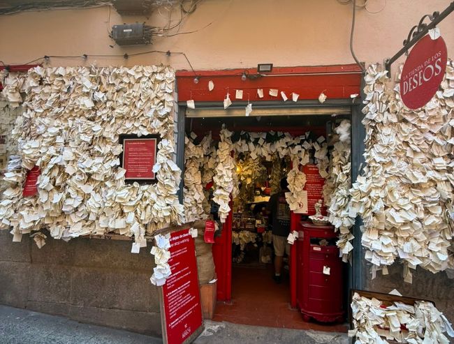The storefront of La Tienda de los Deseos in Madrid, featuring a dark red entrance entirely framed and covered by thousands of small crumpled paper wish notes attached to the exterior walls.