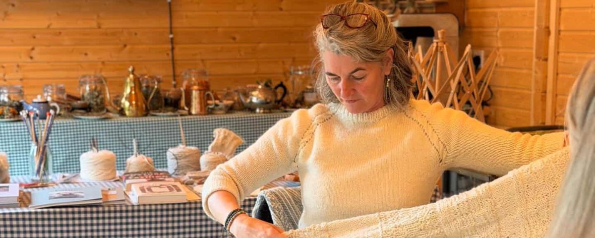 Woman in a cream sweater working with a large piece of white knitted fabric in a rustic studio.