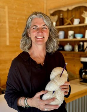 Smiling woman holding a skein of white yarn in a cozy wood-paneled room.