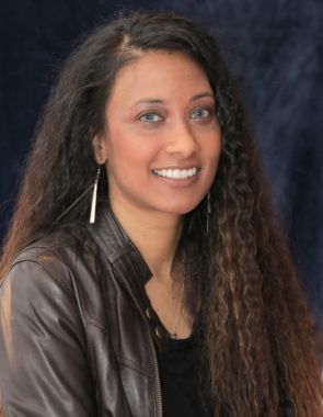 Studio portrait of a smiling woman with long wavy hair wearing a leather jacket.