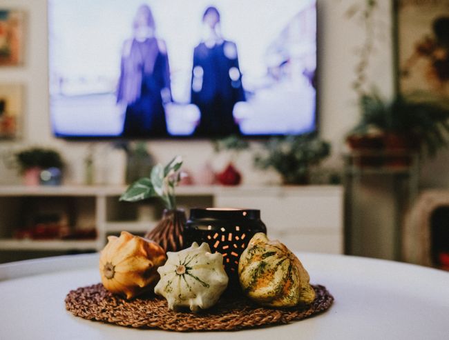 Three decorative autumn gourds and a black candle holder on a coffee table with a blurred TV background.
