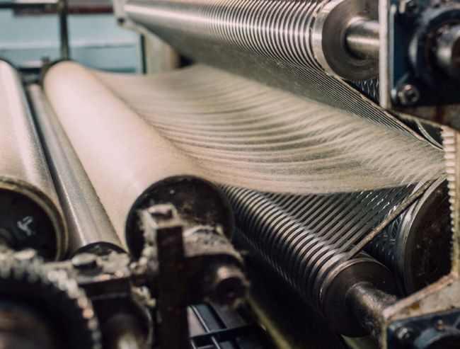 Heavy industrial rollers processing raw white wool fibers inside a textile manufacturing facility.