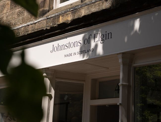 A close-up shot of the white exterior storefront sign for Johnstons of Elgin, featuring the text 