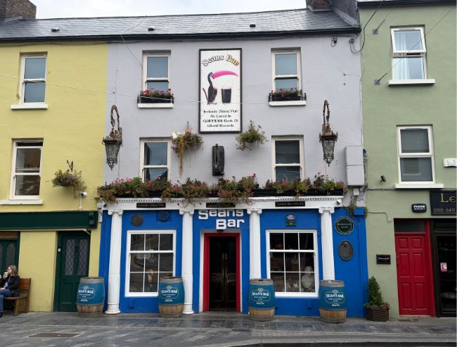 The front facade of Sean's Bar, a traditional Irish pub with bright blue wood framing on the ground floor and grey walls above.